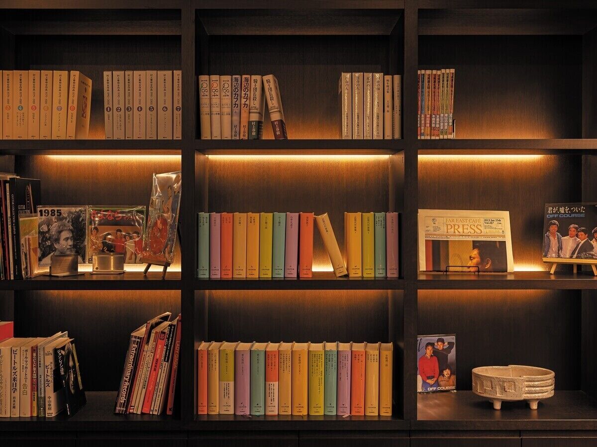 Una estantería con libros y revistas, un cuadro enmarcado y una mesita con una lámpara.