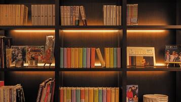 Una estantería con libros y revistas, un cuadro enmarcado y una mesita con una lámpara.