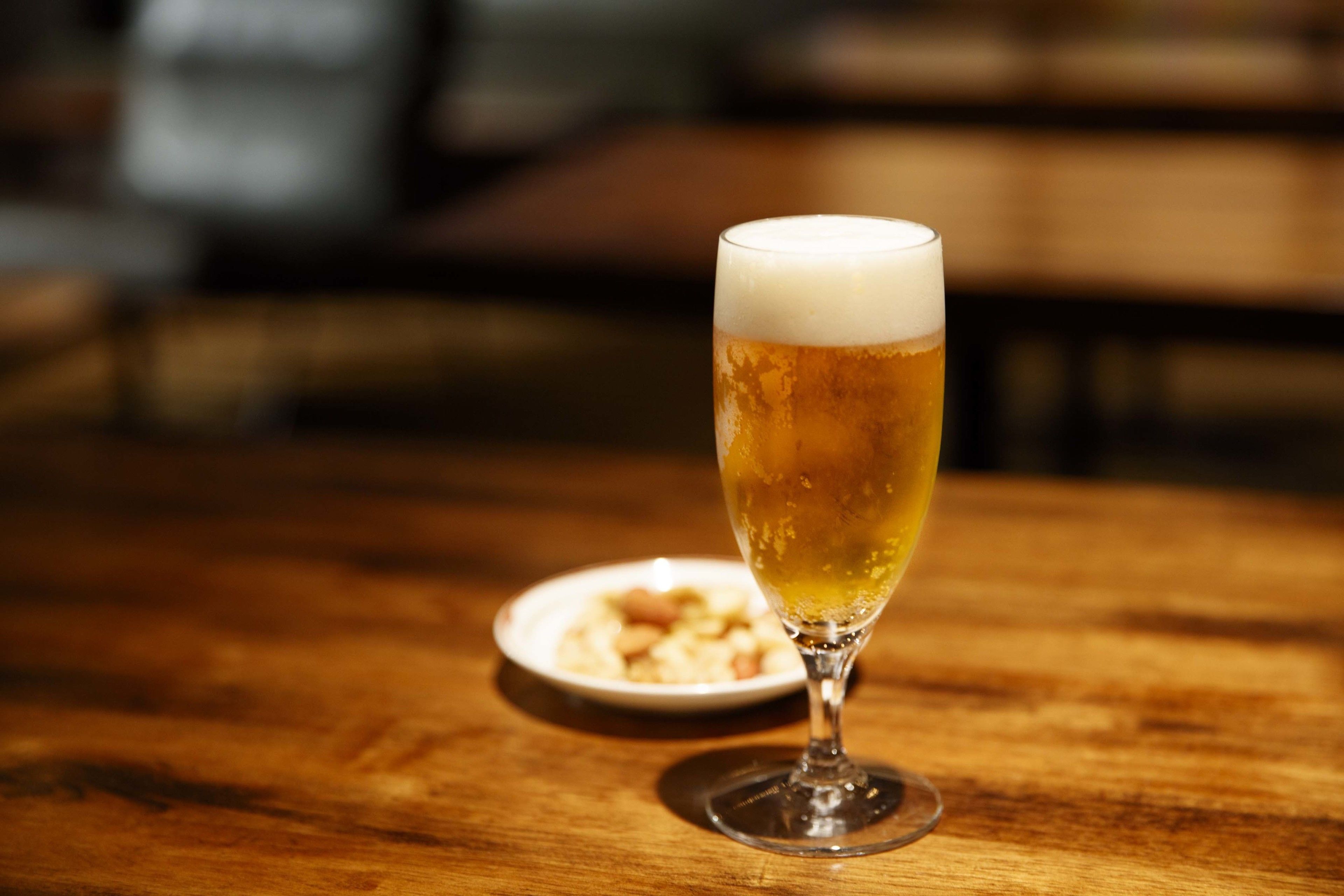 Un vaso de cerveza sobre una mesa de madera, con un fondo desenfocado.