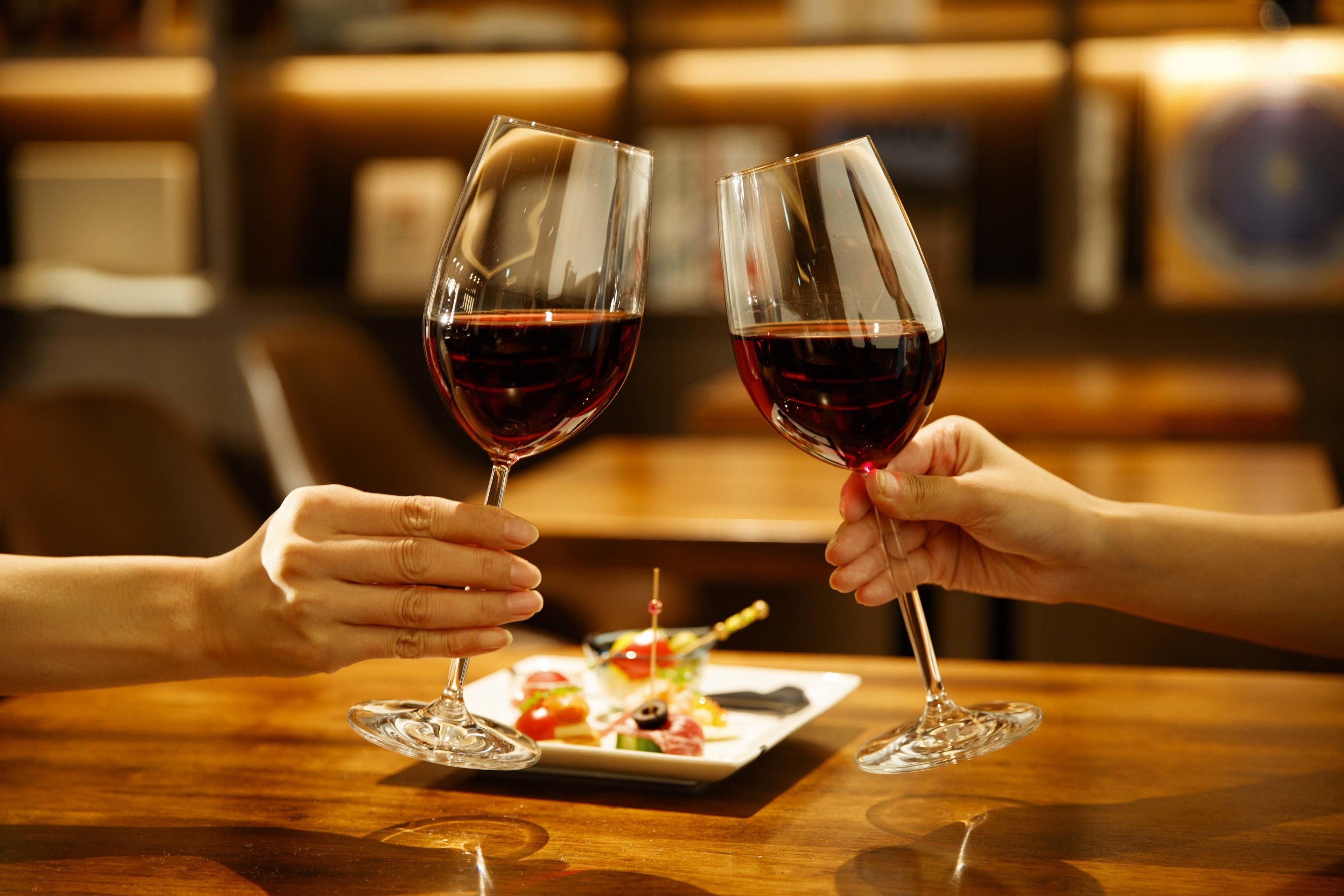 Dos personas brindando con copas de vino sobre un pequeño plato de aperitivos.