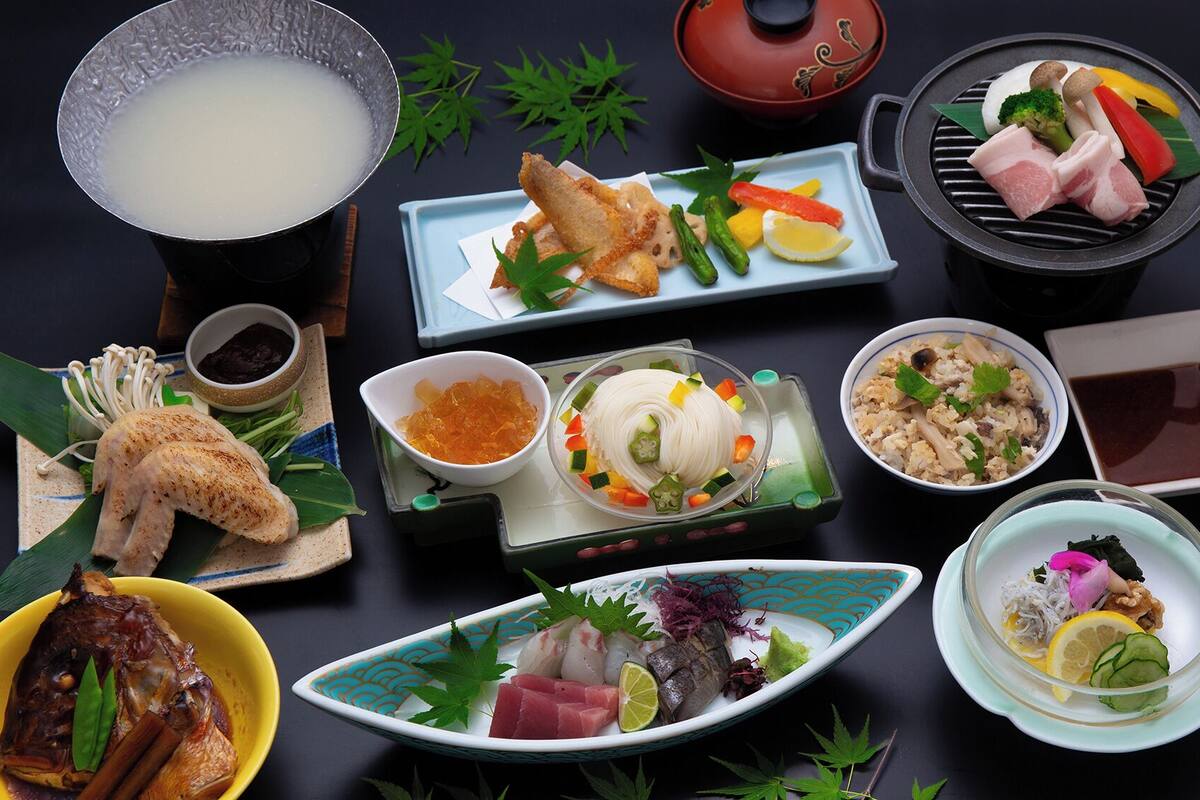 A variety of Japanese dishes including grilled meat, sashimi, and a bowl of soup.