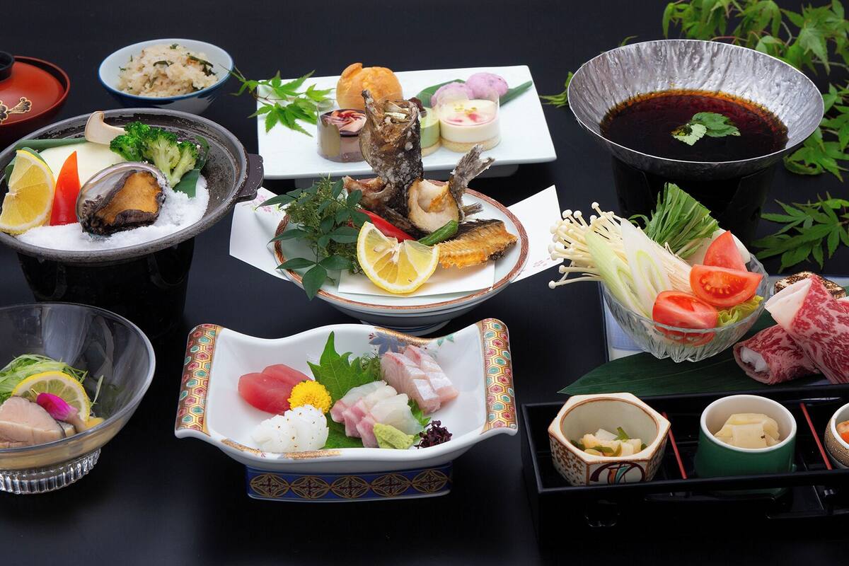 A variety of Japanese dishes including sushi, sashimi, and tempura, arranged on a black table.