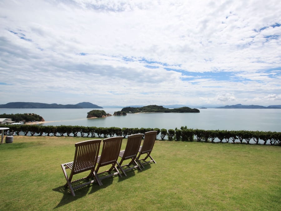 A grassy outdoor area with two wooden chairs facing a body of water and distant islands.