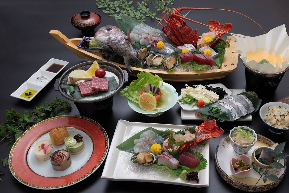 A variety of Japanese dishes including sushi, sashimi, and seafood, arranged on a table with a dark background.