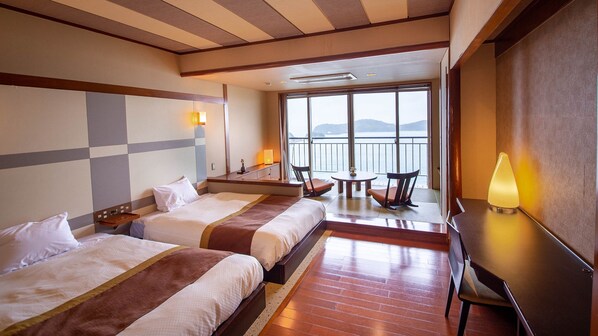 Habitación de hotel con dos camas, un escritorio, una silla y vista al mar.