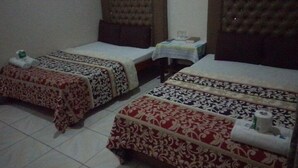 A hotel room with two single beds, each with a patterned bedspread. There is a small table with a lamp and a book on it.