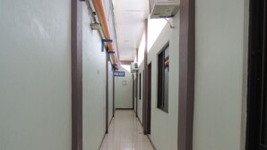 A long, narrow hallway with tiled flooring and walls, a fire exit sign, and a window on the right.