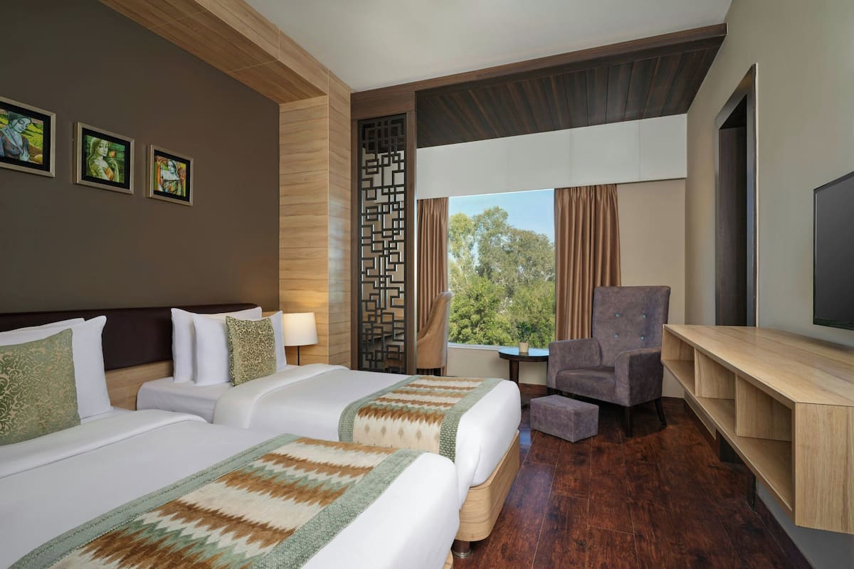 Habitación de hotel con dos camas, televisión, escritorio y vista a árboles.