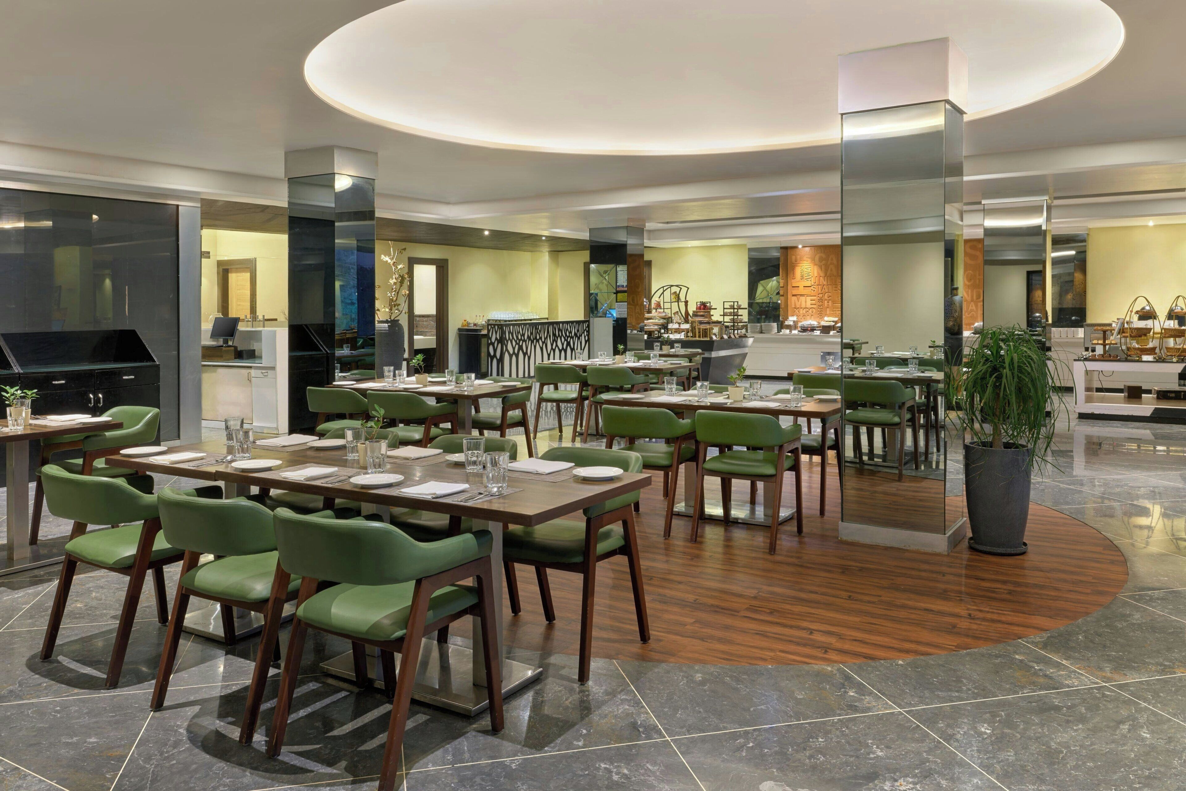 A modern restaurant with green chairs, wooden tables, and a central island.