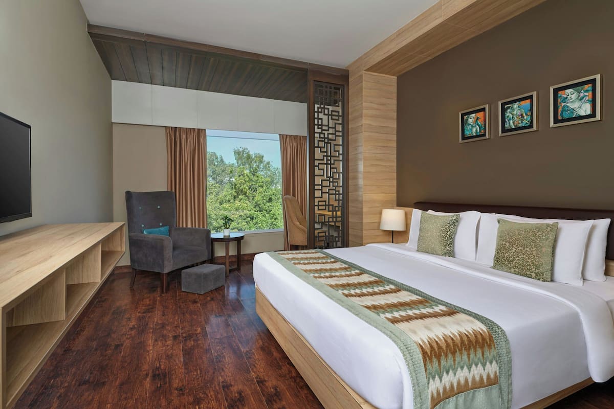 Habitación de hotel con una cama grande, un escritorio, una silla, un televisor y una ventana con cortinas.