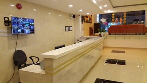 Un área de recepción con mostrador de mármol, televisor montado en la pared y un sofá rojo al fondo.