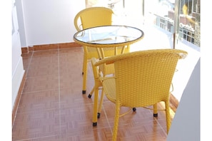 Ein Balkon mit gelbem Korbmöbel, einem Glastisch und einem gefliesten Boden.