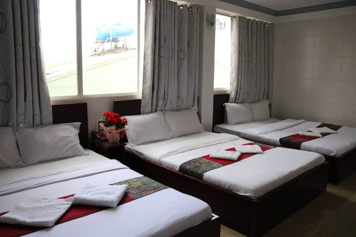 A hotel room with three single beds, a large window with curtains, and a view of the outside.