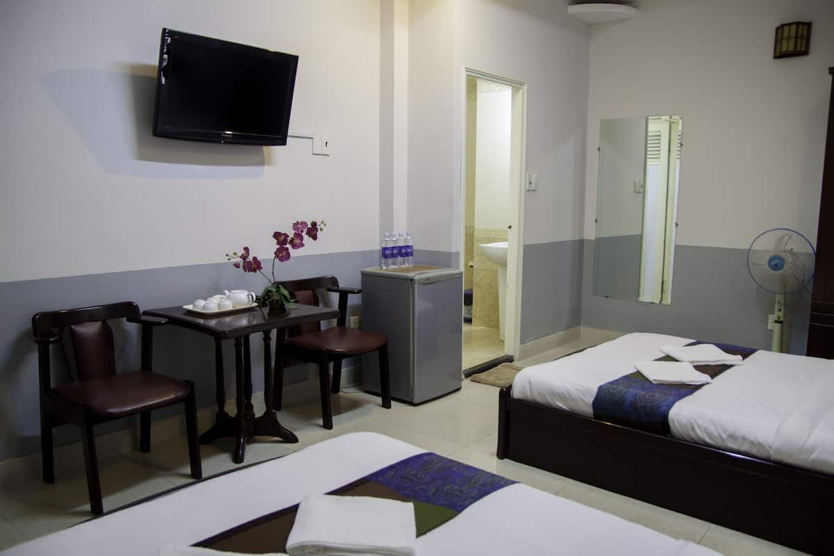 A hotel room with two beds, a desk with chairs, a television, a refrigerator, and a bathroom visible through an open door.