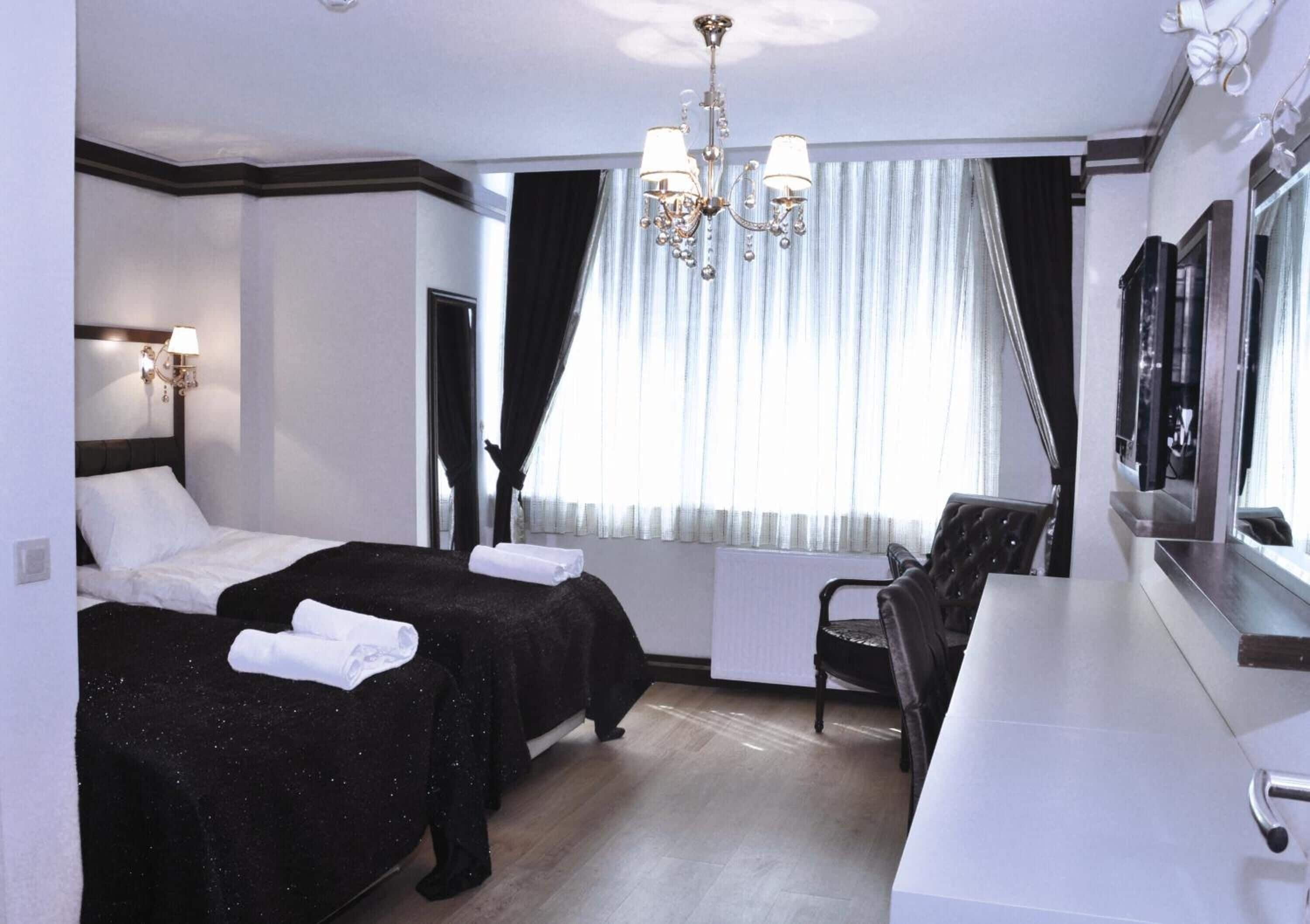 A hotel room with two beds, a desk, a chair, a TV, and a chandelier.
