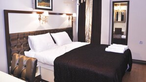 Habitación de hotel con una cama grande, cabecera con diseño acolchado, dos apliques, una araña y un cuadro en la pared, además de un espejo en una esquina.