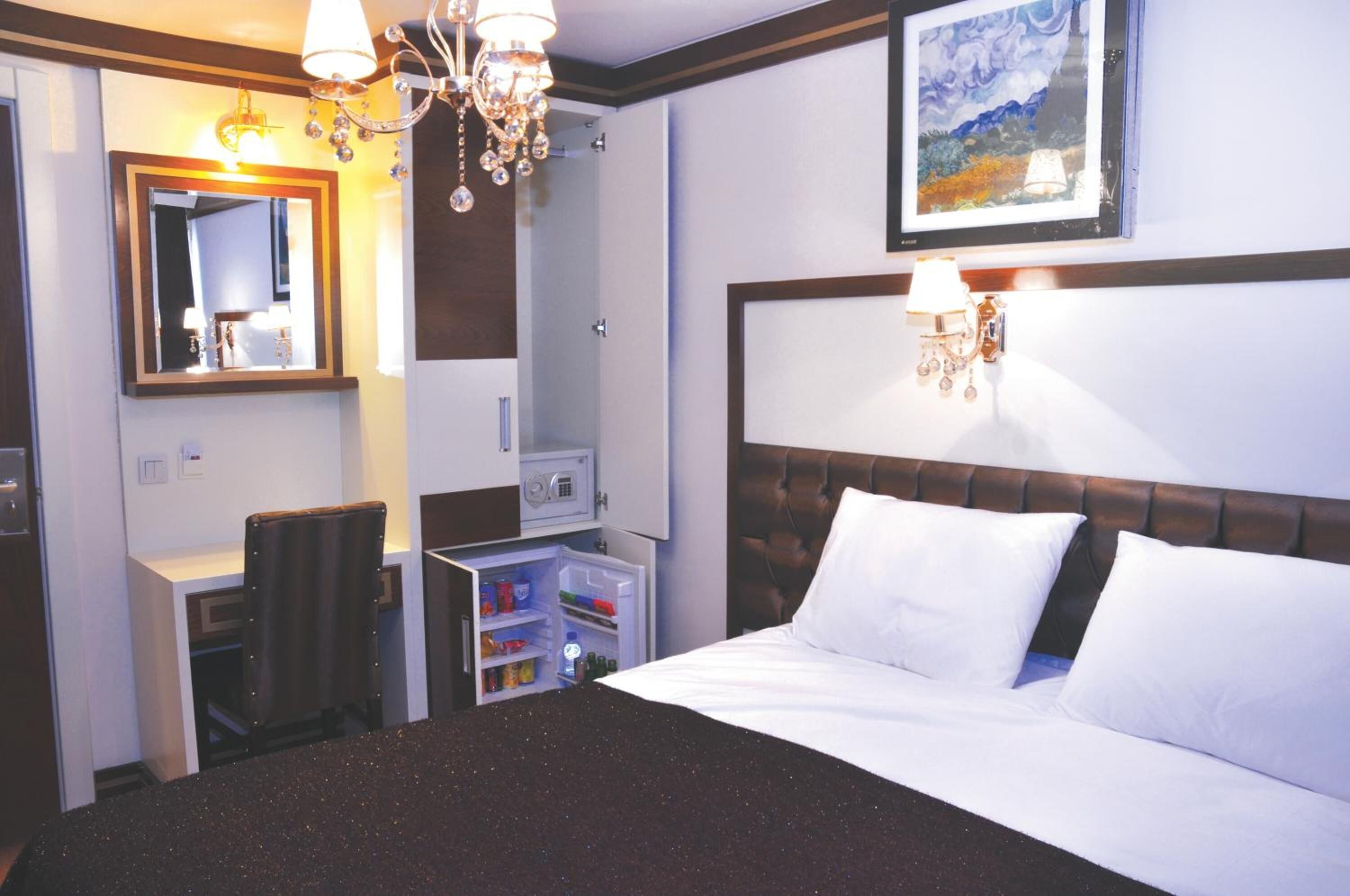 Habitación de hotel con cama, escritorio con silla, armario, espejo y candelabro.