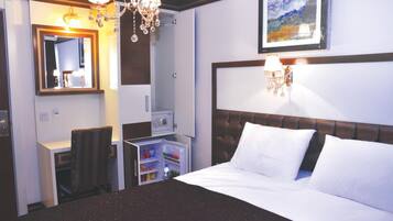 Habitación de hotel con cama, escritorio con silla, armario, espejo y candelabro.