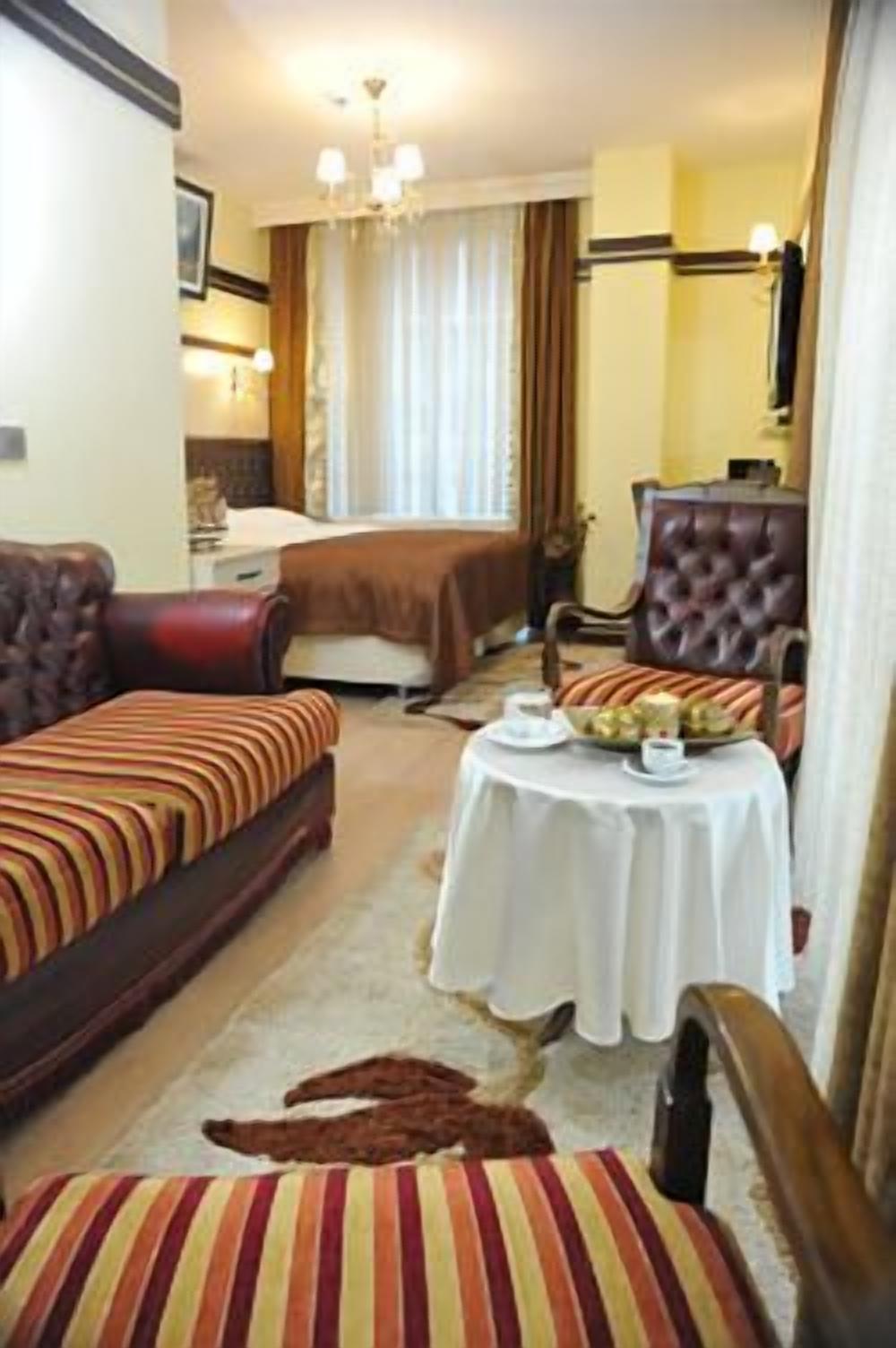 Een hotelkamer met een bed, twee banken, een eettafel met een wit tafelkleed en een kroonluchter.