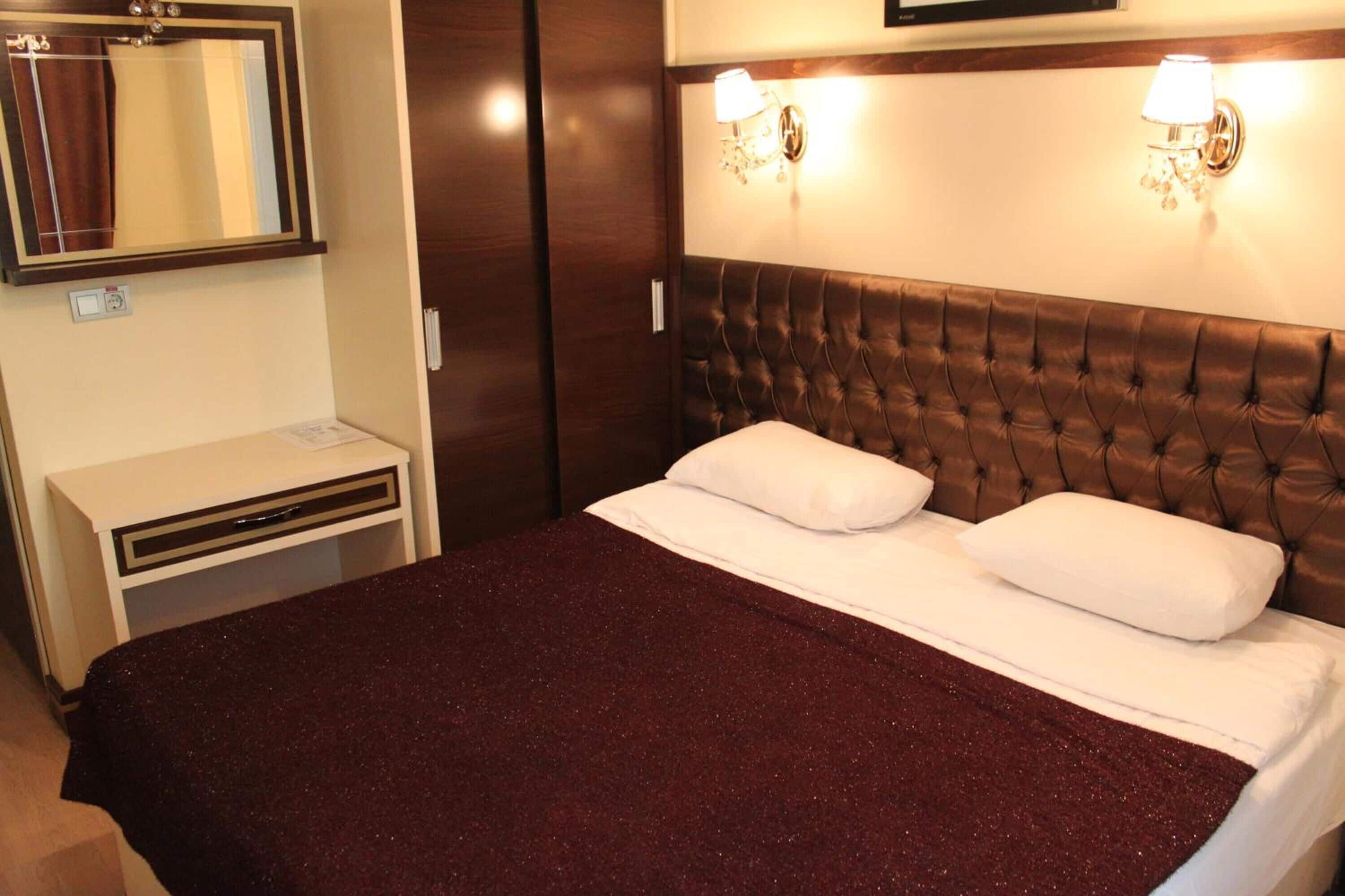 A hotel room with a large bed, a nightstand, a mirror, and wall-mounted lighting.