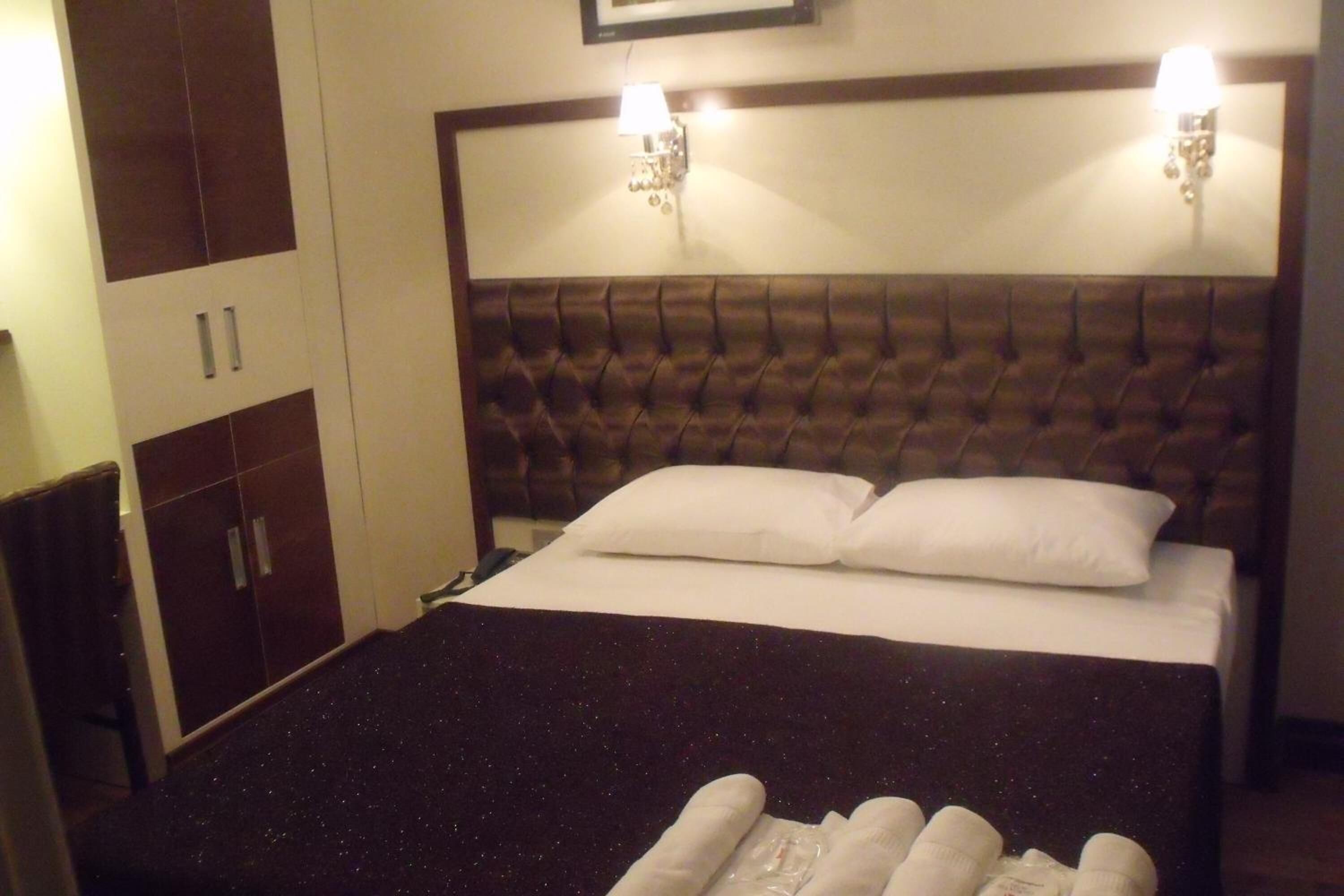 A hotel room with a large bed, two bedside lamps, a headboard, and a wardrobe.
