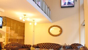 Un salón espacioso con techo alto, una araña, un televisor y sofás de cuero.