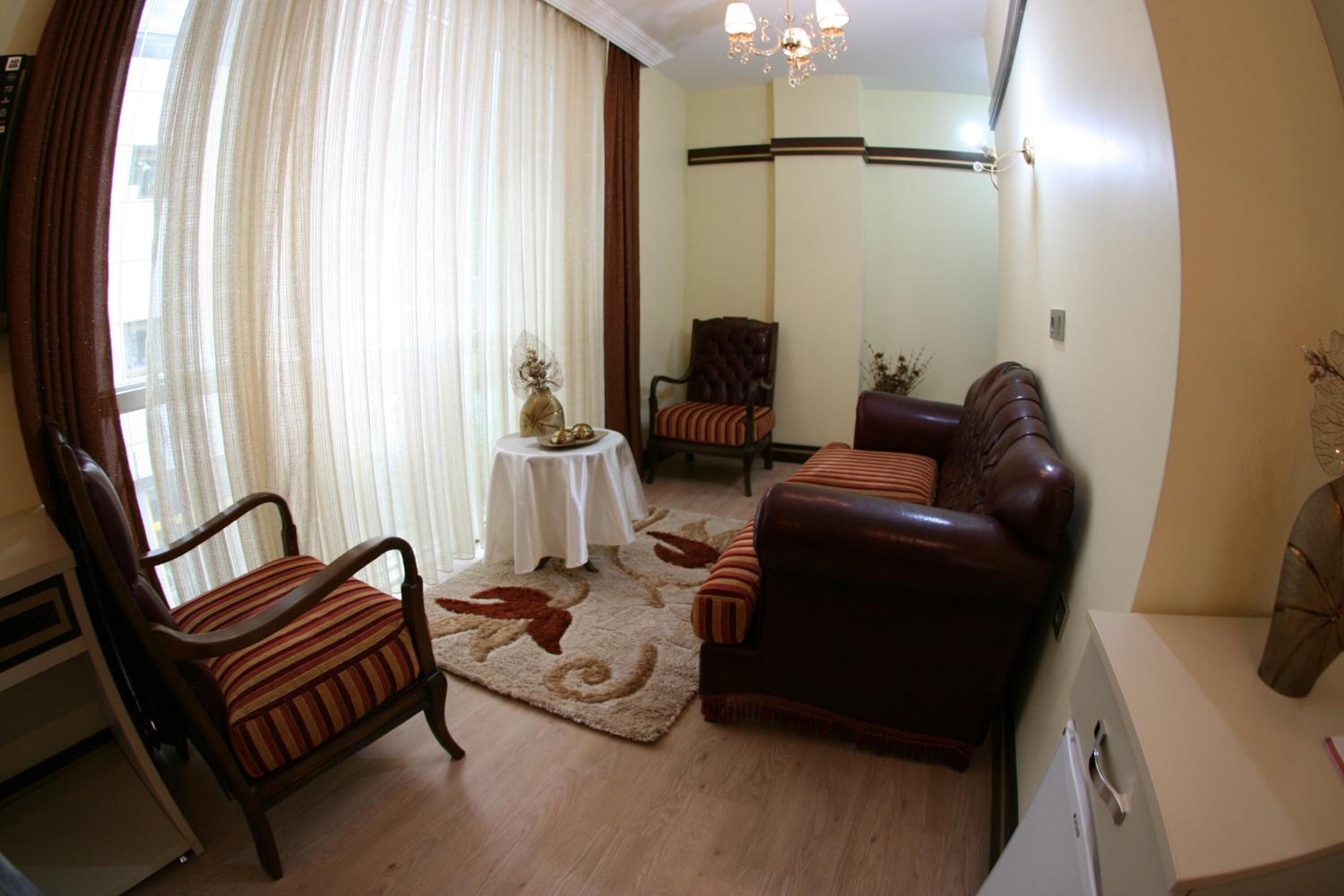 A living room with a brown leather sofa, striped armchairs, a small round table with a vase, and a large window with sheer curtains.