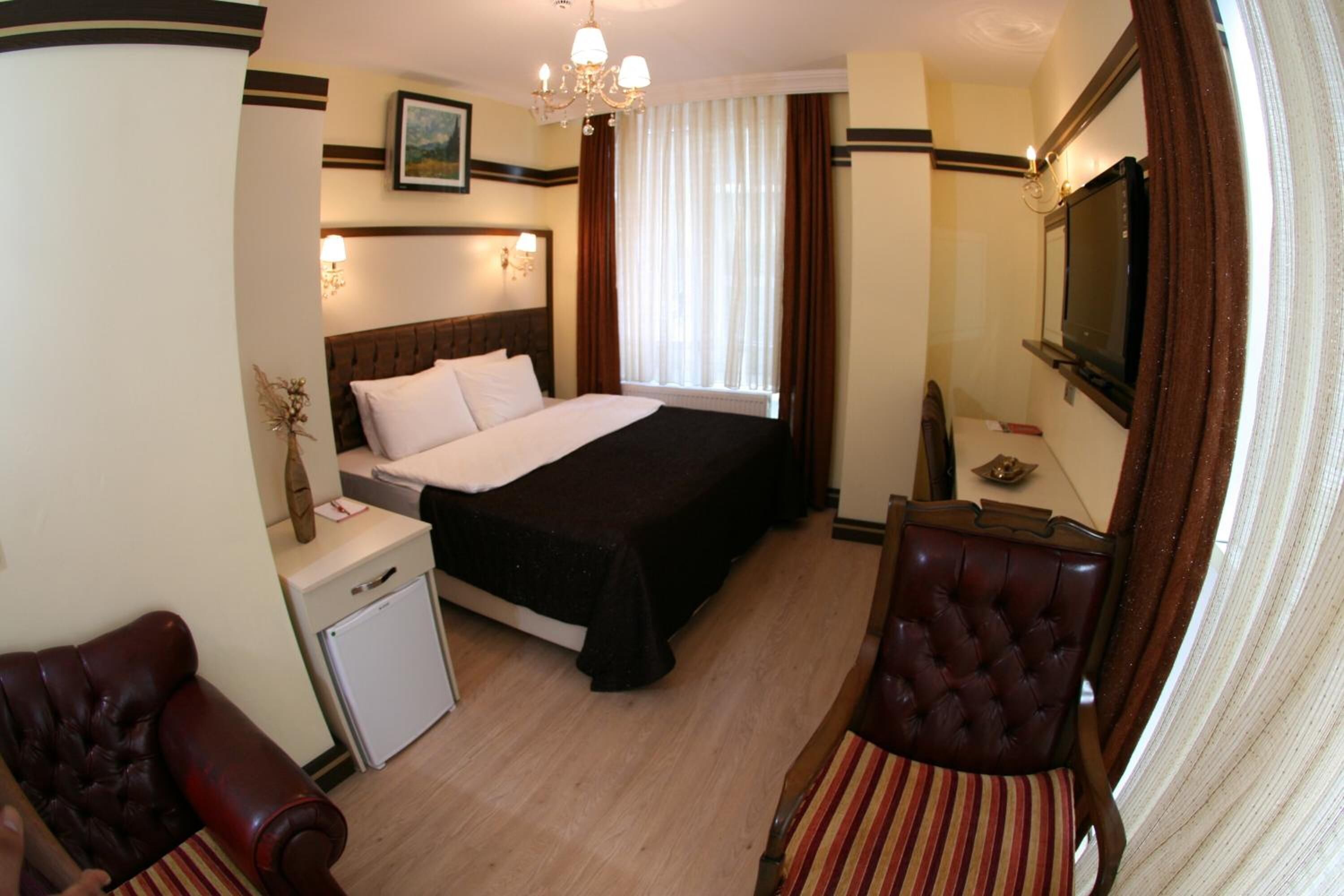 A hotel room with a bed, a television, a desk, a chair, and a small refrigerator.