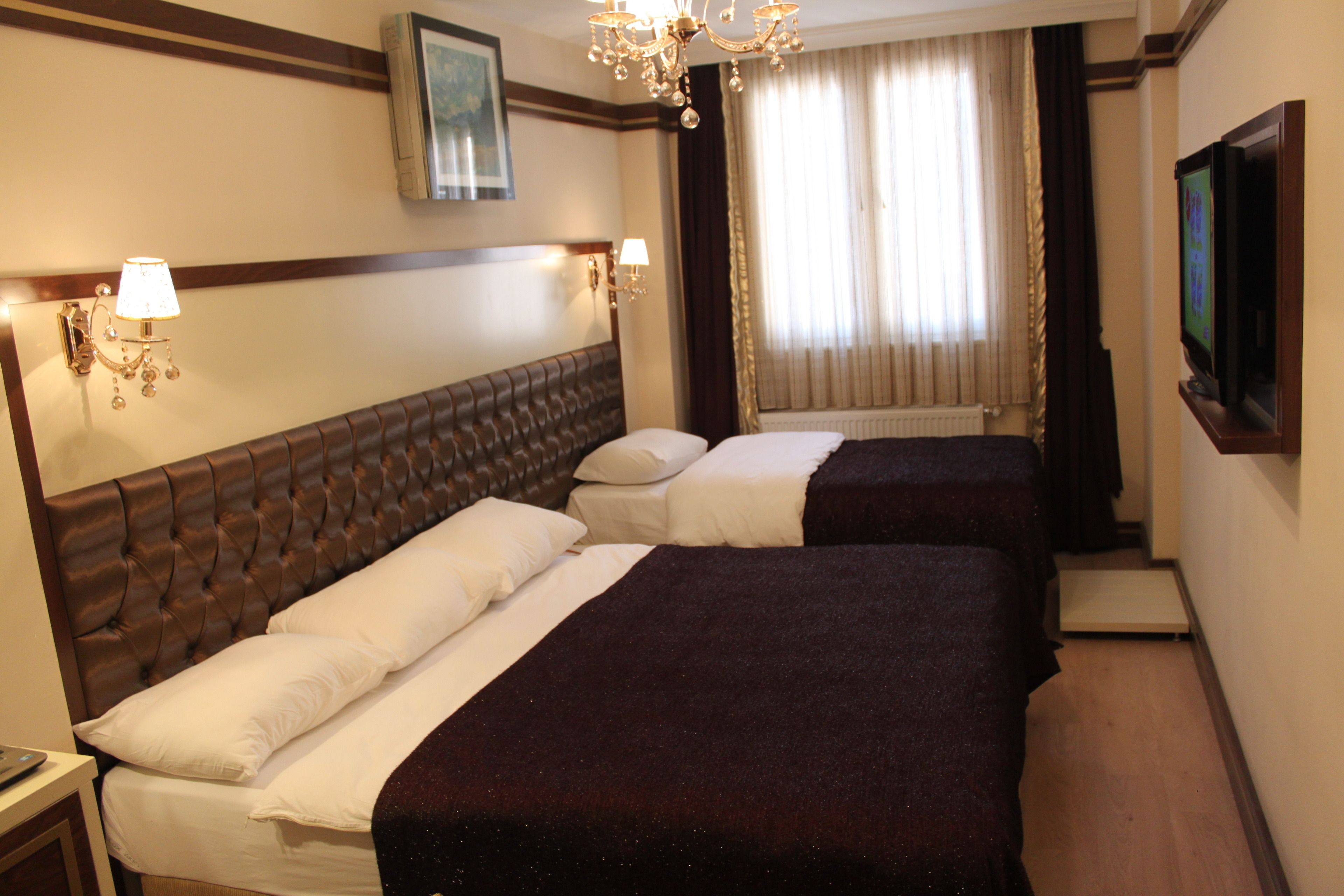Una habitación de hotel con dos camas, un candelabro, un televisor y una ventana con cortinas.