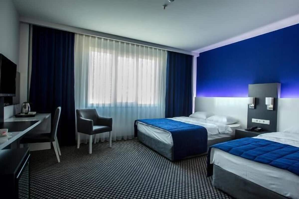 A hotel room with two beds, a desk, a chair, a TV, and a window with curtains.