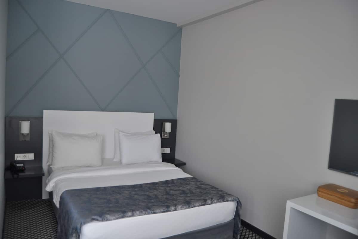 A hotel room with a bed, bedside tables, a nightstand, a lamp, a TV, and a small wooden box.