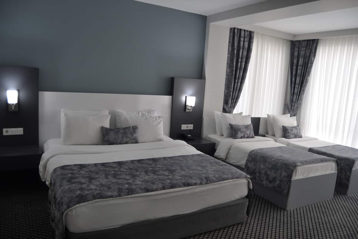 A hotel room with a large bed, two bedside tables, a nightstand, and a window with curtains.