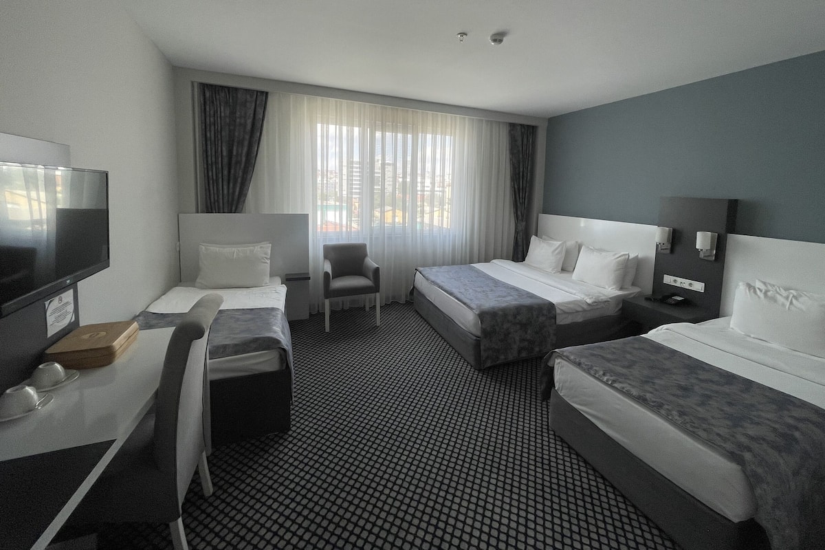 A hotel room with two beds, a desk with a TV, a chair, and a large window with curtains.