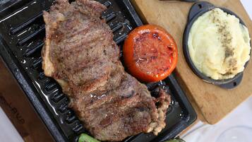 A steak, a grilled tomato, and mashed potatoes on a grill pan.