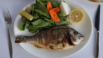 Un piatto con pesce alla griglia, insalata mista, fettine di carota, limone e sottaceti.