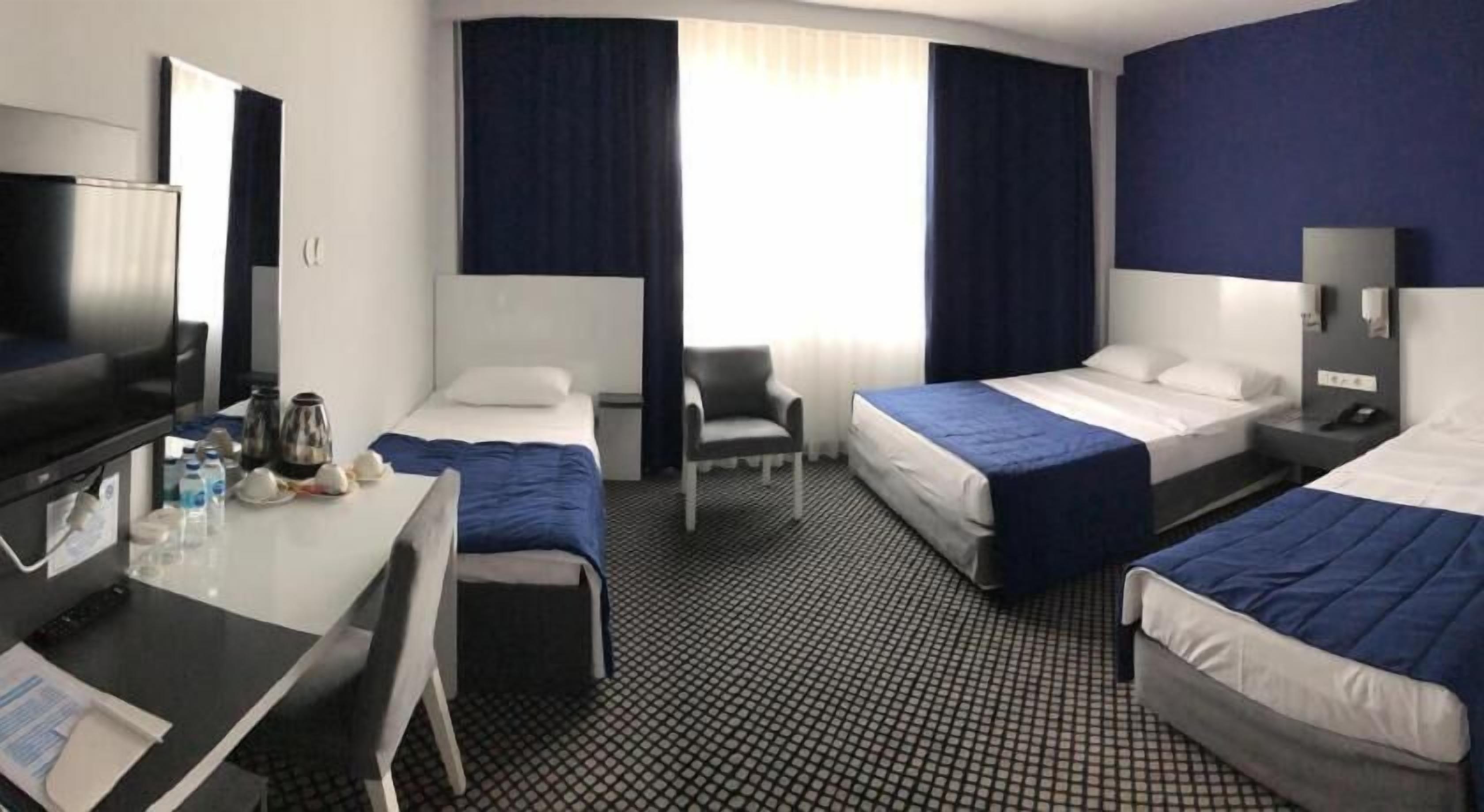A hotel room with two beds, a desk with a computer, a chair, a TV, and a window with curtains.
