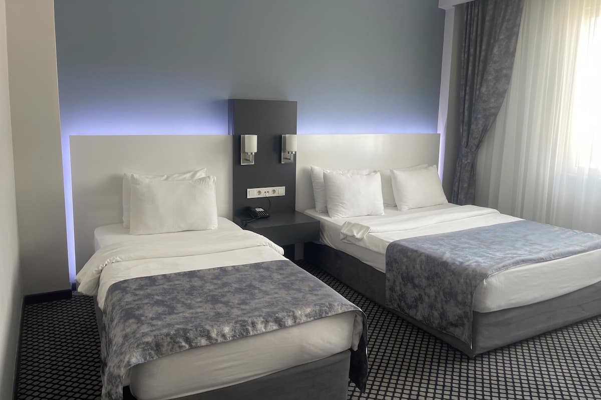 A hotel room with two beds, a nightstand, a phone, and a wall-mounted light fixture.