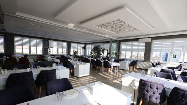 Un comedor espacioso con varias mesas dispuestas para el servicio, amplias ventanas que ofrecen vistas y un diseño de techo moderno.
