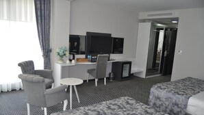 Una habitación de hotel con una cama, dos sillones, un escritorio pequeño con una computadora, un televisor y un espejo.