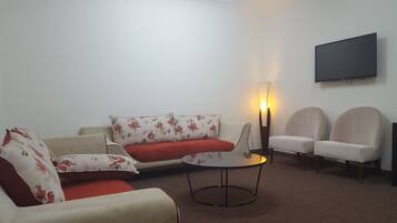 Sala de estar com sofá, duas poltronas, mesa de centro, abajur e televisão na parede.