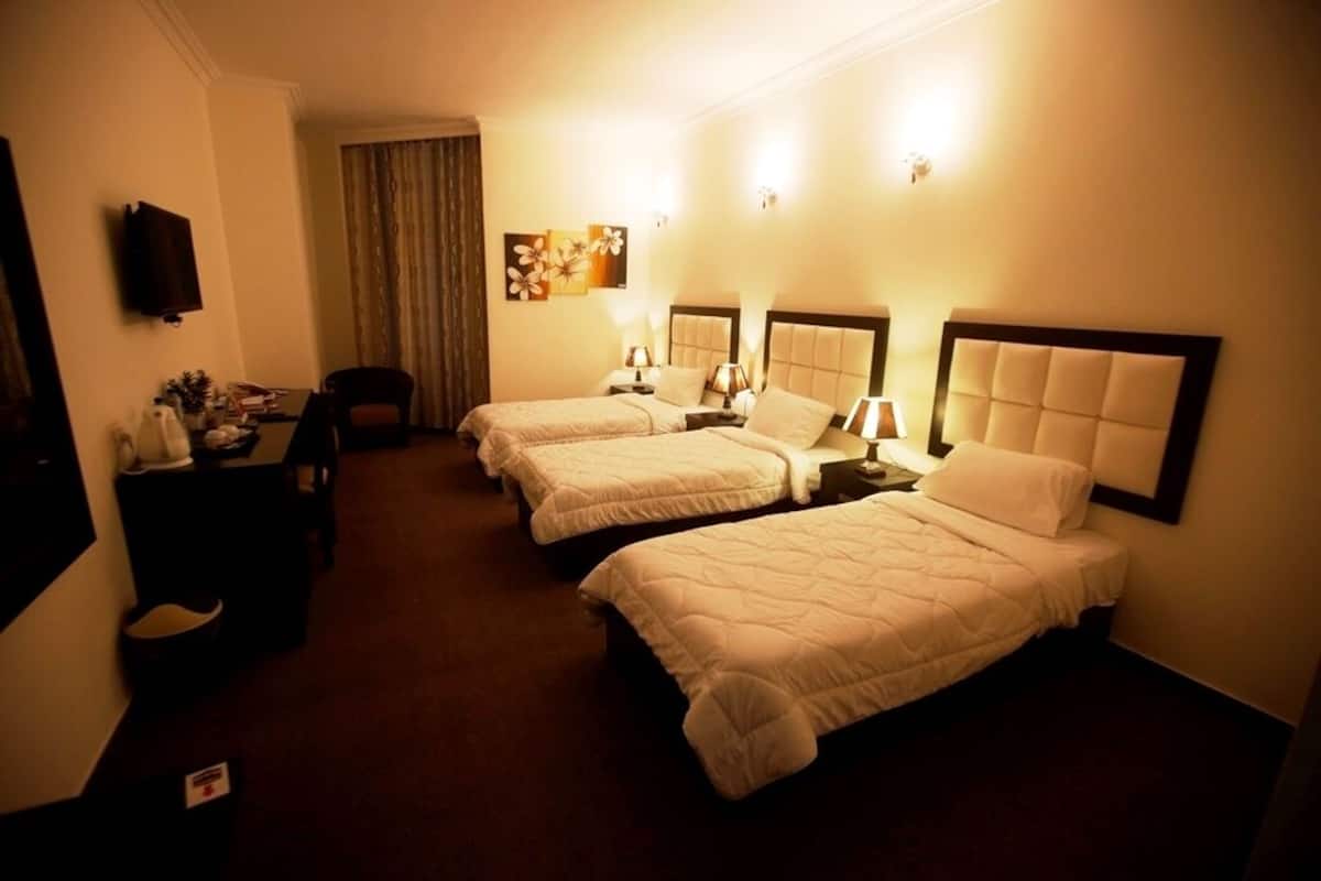 Una habitación de hotel con tres camas, un escritorio con una silla, una televisión y un cuadro en la pared.