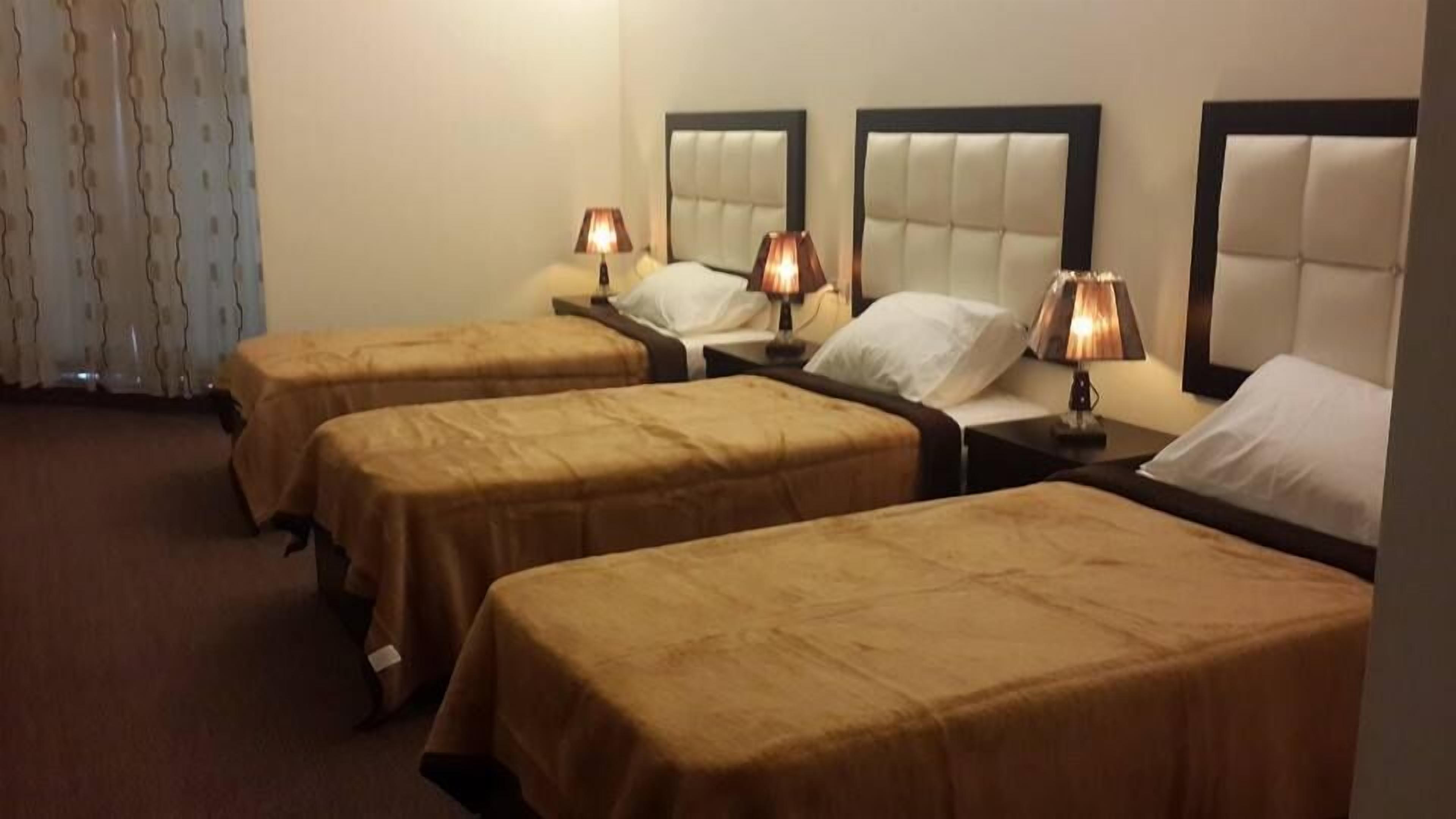 A hotel room with three single beds, each with a headboard and bedside tables.