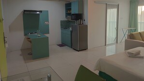A compact hotel room with a kitchenette, a bed, a chair, and a sliding glass door to the outside. -  Santorini Hotel (Miri)