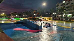 Una pista de skate nocturna con rampas y un edificio al fondo.