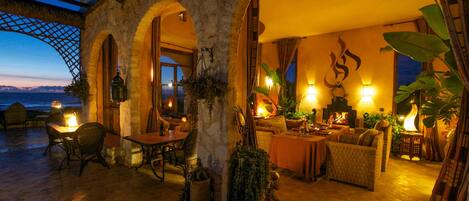 A cozy, well-lit lounge area with stone arches, comfortable seating, and a view of the sea.
