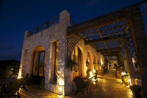 Un patio al aire libre con muros de piedra, arcos de madera y mesas y sillas.