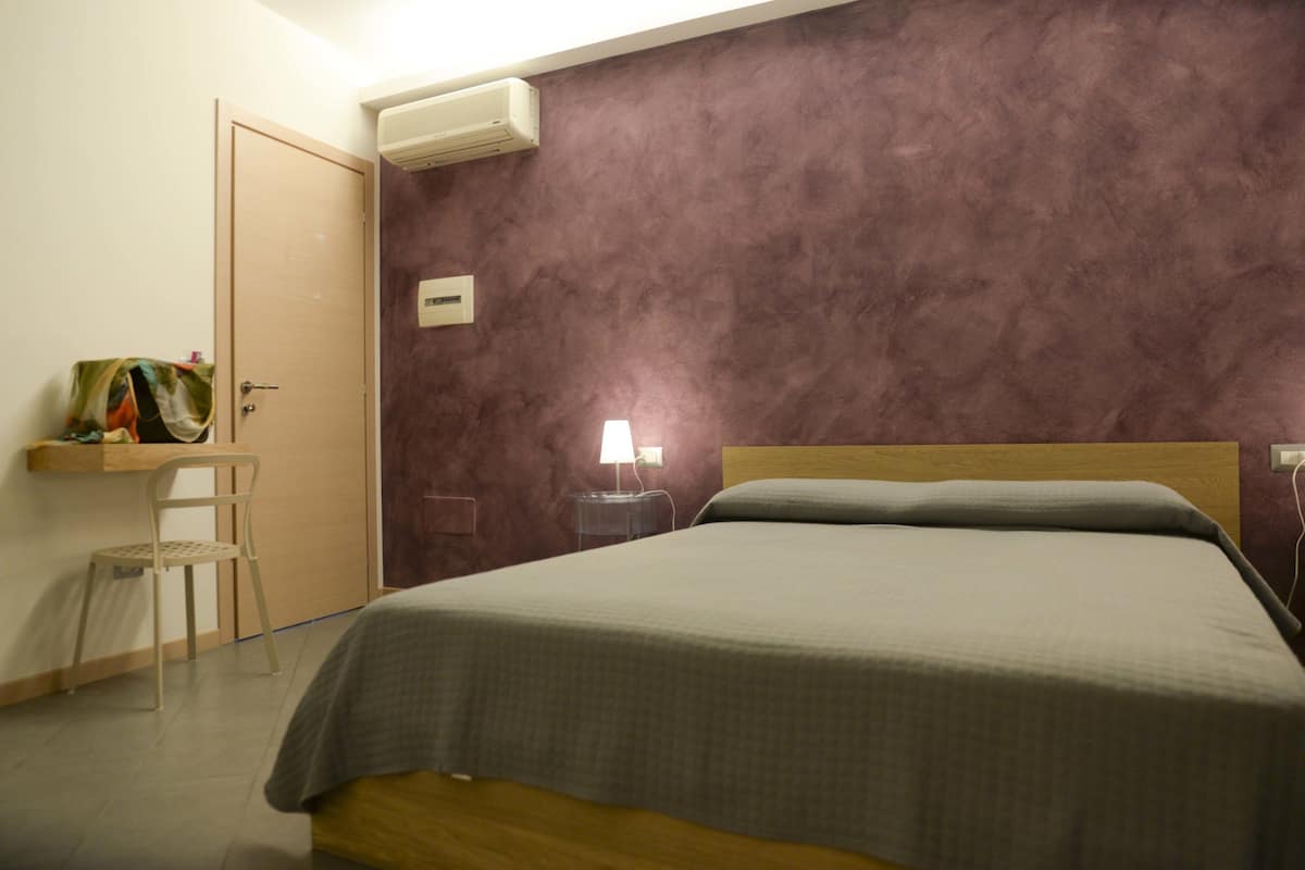 Une chambre à coucher comprenant un lit, une chaise, un bureau et un climatiseur fixé au mur.