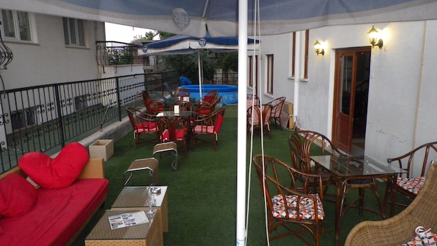 An outdoor patio with a red sofa, wicker chairs, a glass table, and a blue pool in the background. - Öz Mert Hotel (Konyaalti)