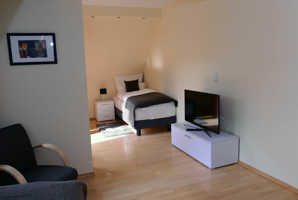 Un dormitorio con cama, mesita de noche, televisión y una silla.