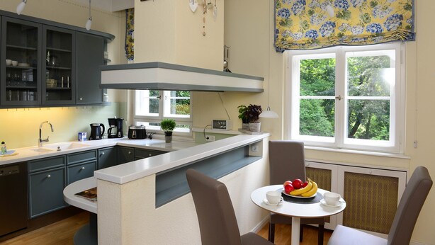 A modern kitchen with a central island, built-in cabinets, and a window with a view of greenery. - Residenz am englischen Garten (Munich)